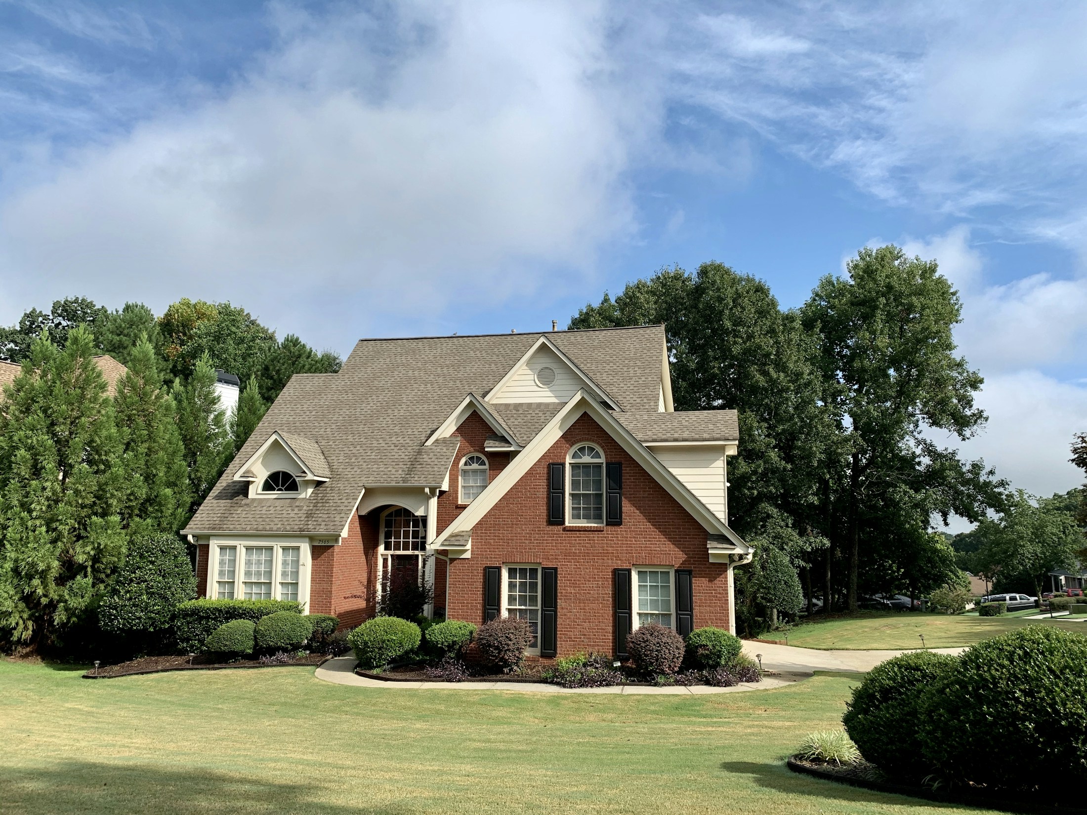 A two-storey red brick house with cream gables, arched dormer windows and a wide clipped lawn.