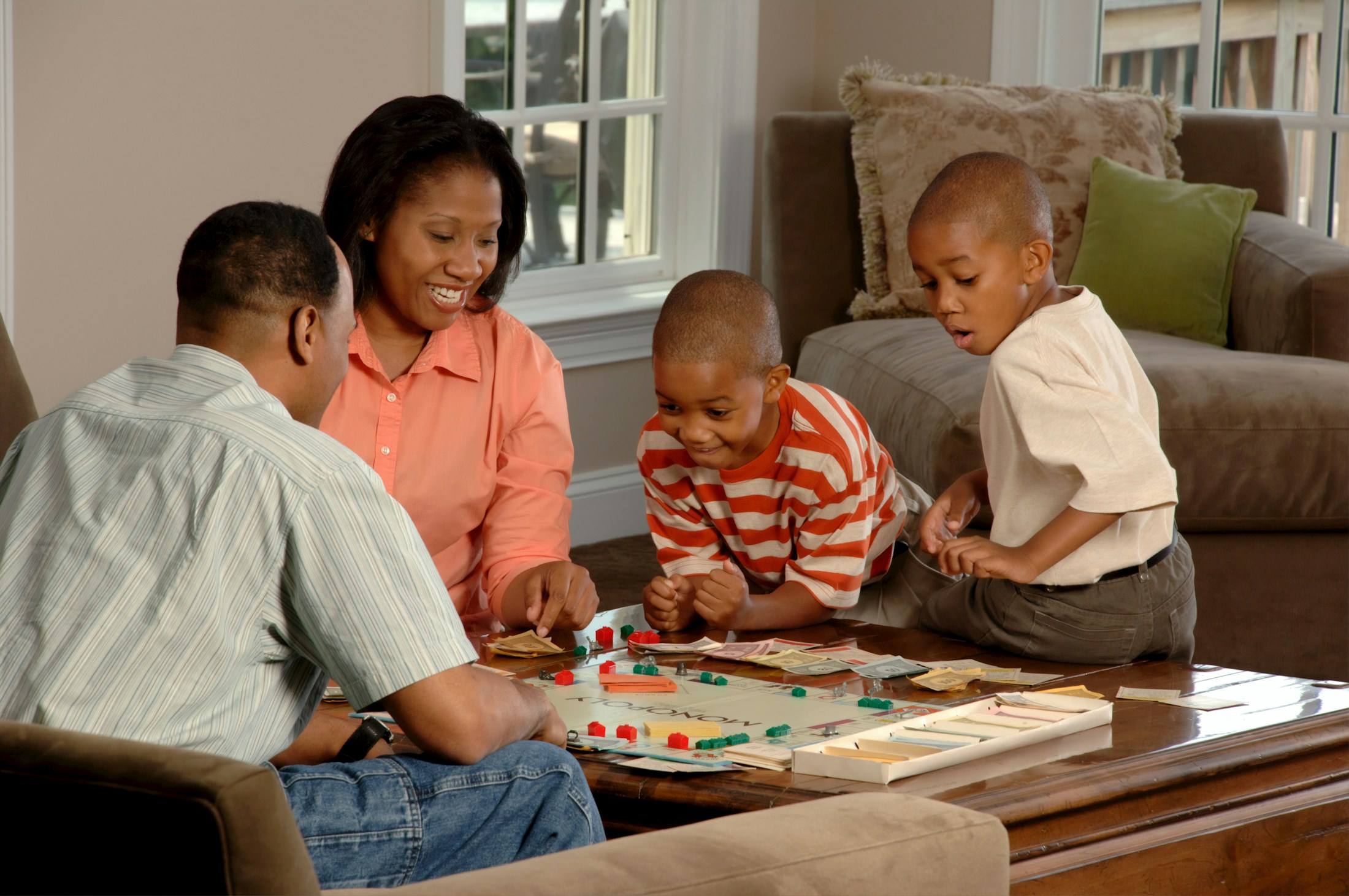 Two parents and two children leaning over a board game on a living-room coffee table.